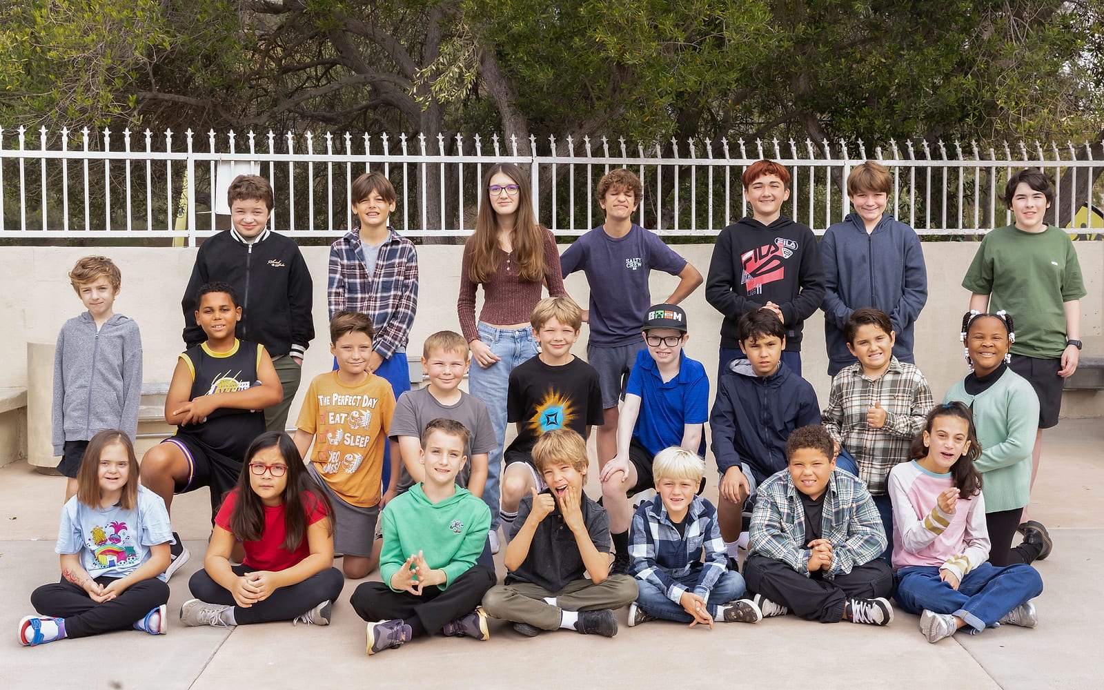 Group photo of LINKS students, from elementary to high school age, sitting and standing together outdoors in front of a white fence