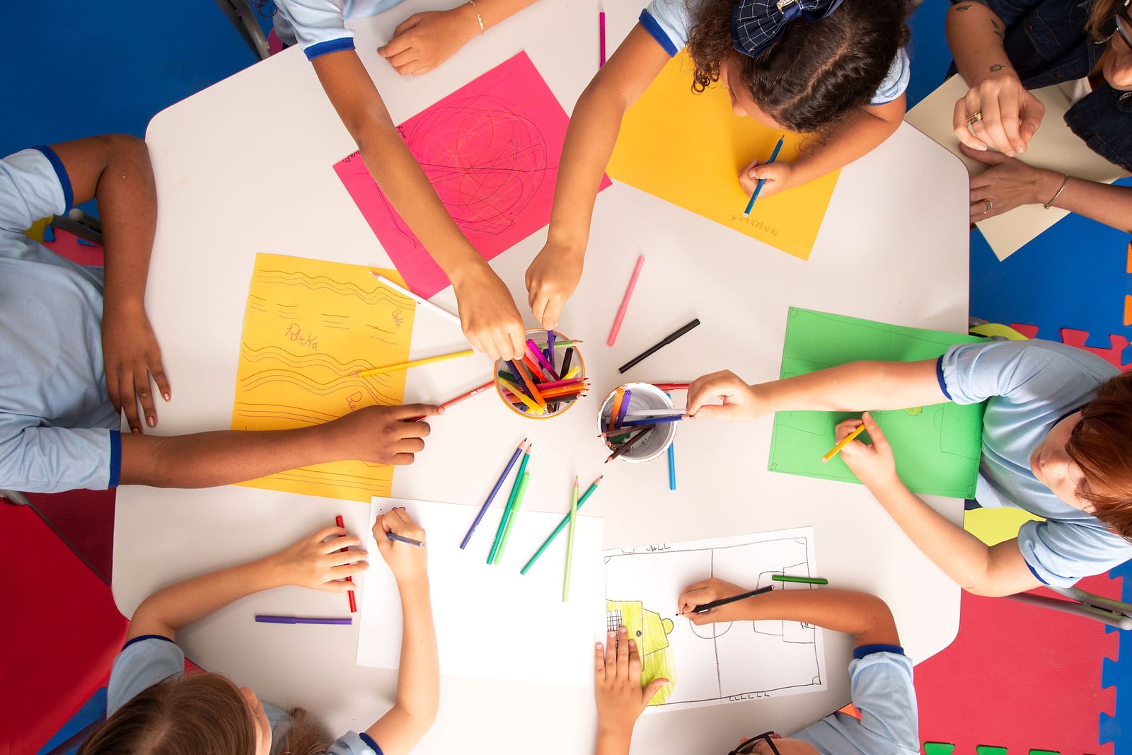 Overhead view of students in uniforms drawing with colored pencils at a table