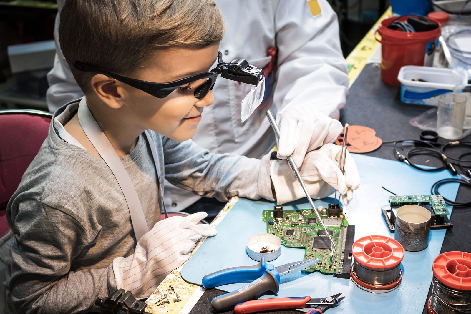 A student wearing safety glasses and gloves soldering an electronic circuit board