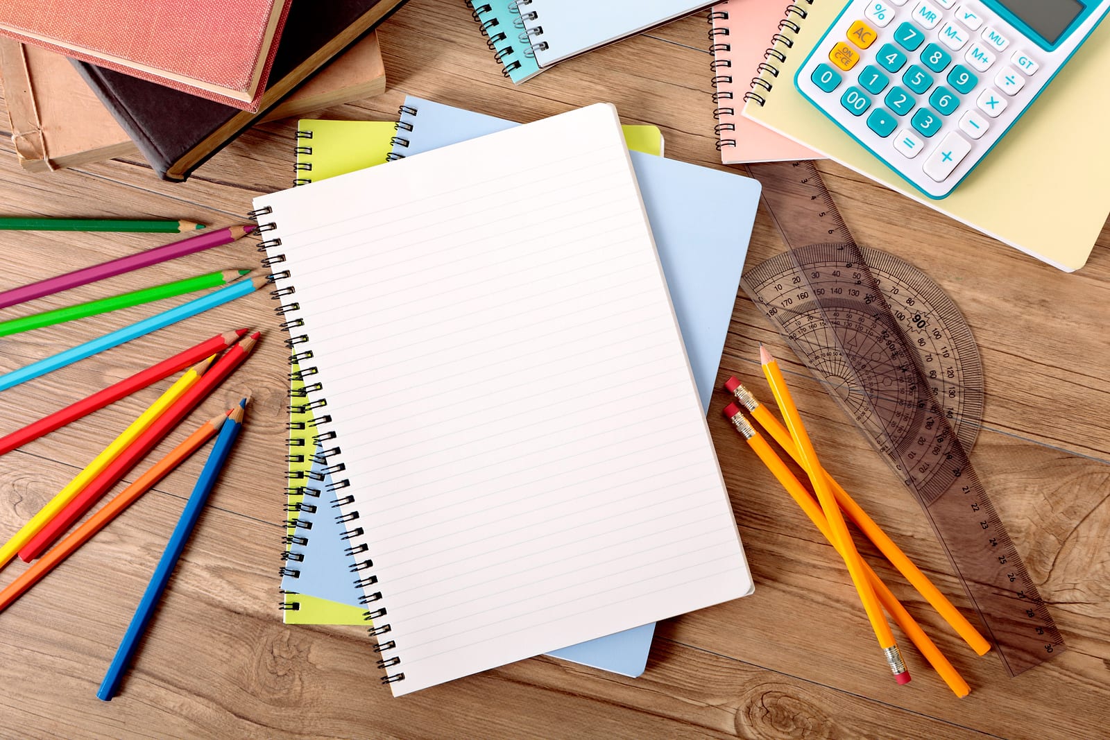 Flat-lay of notebooks, pencils and a calculator on a wooden desk